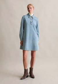 Light blue denim dress with long sleeves, collared neck, button placket, and mid-thigh length. Worn with gray ankle boots.