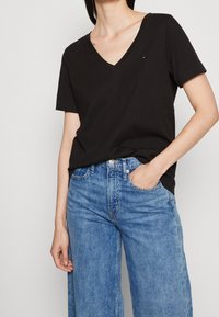 Sort bomulds T-shirt med korte ærmer og V-hals i en afslappet pasform. Der er et lille mærke-logo på brystet, og den er kombineret med lyseblå denimjeans.