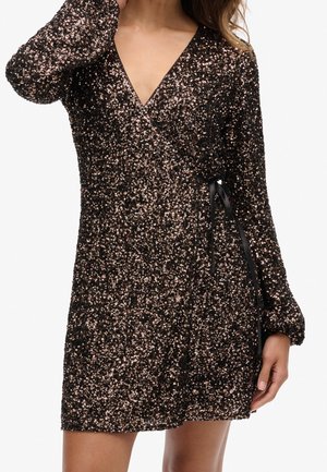 Robe noire avec des sequins rose gold, décolleté en V profond, manches longues, design enveloppant et lien sur le côté. Longueur courte, surface texturée.