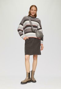 Sweter w paski w kolorze szarym, białym i koralowym, w połączeniu z ciemnoszarym spódnicą z kordurowej tkaniny. Szara torebka crossbody i beżowe botki za kostkę z czarnymi podeszwami.