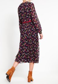 Blumendruck-Midikleid mit langen Ärmeln, navyfarbener Hintergrund, elastischem Taillenbund und plissiertem Rock. Kombiniert mit braunen Stiefeletten.