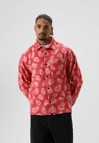 Rood flanellen overhemd met wit paisley patroon, knoopsluiting en een borstzak. Heeft lange mouwen, een losse pasvorm en zwarte knopen.