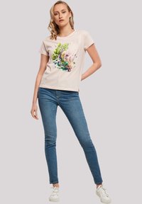 Kurzarm-T-Shirt in Hellrosa mit einem bunten Blumenmotiv. Kombiniert mit blauen Skinny-Jeans und weißen Sneakers.