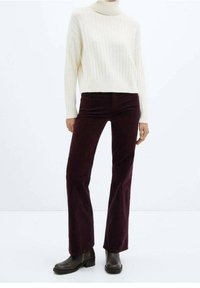 Pull en maille côtelée crème avec col roulé et manches longues, associé à un pantalon évasé en velours côtelé bourgogne. Des bottines brunes complètent la tenue.