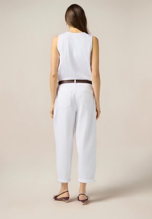 Witte mouwloze top gecombineerd met losse, witte broek en een bruine riem. Kenmerkt zich door opgerolde manchetten en een minimalistisch ontwerp.