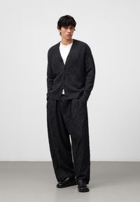 Mörkgrå stickad cardigan med V-ringning och knäppning, i kombination med svarta, strukturerade vida byxor och svarta slip-on skor.