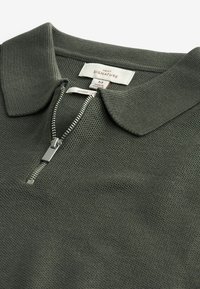 Mörkgrön polo skjorta med en strukturerad väv, har en dragkedja vid halsen och en vikbar krage. Inkluderar en vävd etikett för märke och storlek.