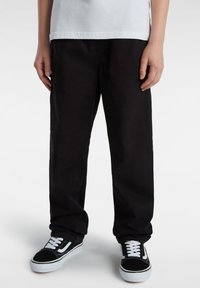 Zwarte katoenen broek met een relaxed fit, voorzien van standaard zakken. Gepaard met zwart-witte vanschoenen. Witte t-shirt zichtbaar erboven.