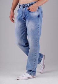 Hellblaue Jeans aus Denim mit lockerer Passform, die eine ausgewaschene Optik, Gürtelschlaufen und zwei Vordertaschen aufweisen. Kombiniert mit weißen Sneakers.