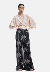 Lichtroze cropped top met een knoopdetail, gecombineerd met zwarte wijde broek met witte borduursels van palmbomen. Zachte stoftextuur.