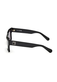 Gafas de sol negras con montura gruesa y varillas rectas. Lentes oscuros y detalle de marca dorado en el costado. Textura de plástico suave.
