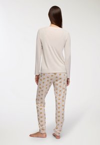 Maglietta a maniche lunghe beige chiaro con una texture morbida, abbinata a pantaloni crema con una stampa animale ripetuta e giocosa, progettati per il massimo comfort.