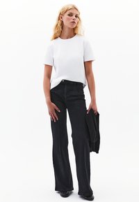 Valkoinen lyhythihainen t-paita yhdistettynä korkeavyötäröisiin mustiin leveälahkeisiin farkkuihin. Asusteissa on huomaamatonta ommeltua yksityiskohtaa ja rento istuvuus.