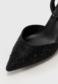 Chaussure slingback à bout pointu noir, fabriquée en matière texturée ornée de perles noires brillantes, dotée d'une sangle élégante et d'une doublure intérieure lisse.
