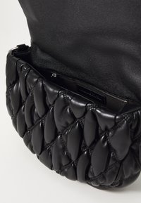 Black leather handbag with a quilted design, featuring a zipper closure and a smooth interior. Soft texture and rounded edge detailing.