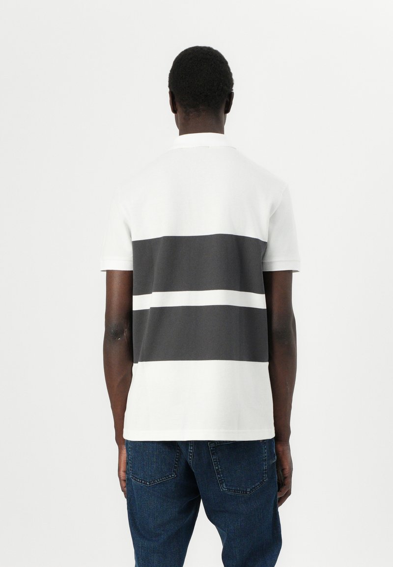 T-shirt polo à manches courtes avec un design rayé blanc et gris foncé, fabriqué en coton, avec un col classique et un ourlet droit.