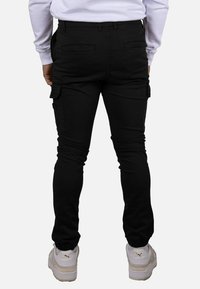 Pantalones cargo negros con un corte ajustado, que cuentan con bolsillos laterales, puños elásticos y una textura de tela suave. Combinados con zapatillas blancas.