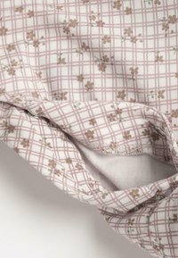 Tissu blanc avec un motif en grille rose, comportant de petites fleurs brunes et des accents verts. Texture douce, bordures froncées et couture sécurisée.