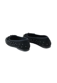 Zapatos planos negros con pequeñas tachuelas plateadas y una decoración de lazo en la parte frontal, exhibidos sobre un fondo blanco.