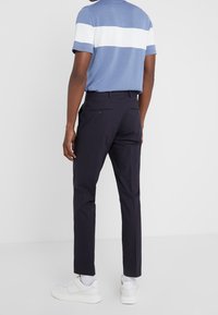 Mörkblå byxor med slim fit, tillverkade av lättviktsmaterial. Har två bakfickor och en knappdetalj, kombinerade med en blå och vit randig skjorta.