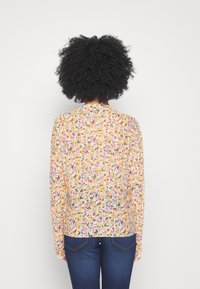 Bloemenblouse met lange mouwen in pasteltinten met kleine bloemen op een lichte achtergrond. Lichtgewicht stof met een ronde halslijn en een ontspannen pasvorm.