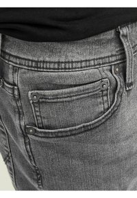 Κοντινή λήψη από τσέπη γκρι τζιν παντελονιού με μεταλλικά τσιμπιδάκια και μαύρη μπλούζα χωμένη στη μέση.