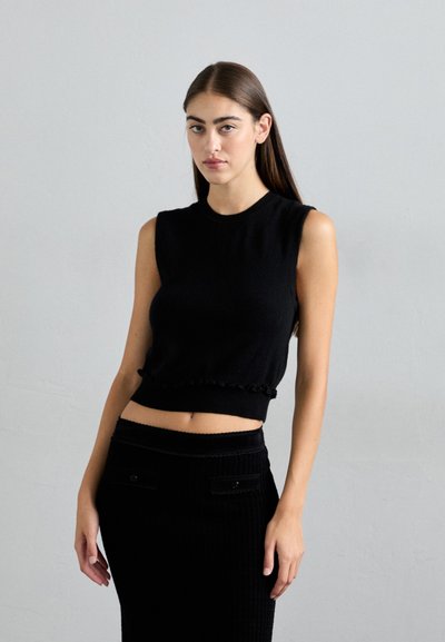 Top negru fără mâneci din tricot, cu un tiv ondulat, având un finisaj texturat și detalii clopot. Asortat cu o fustă corespunzătoare.
