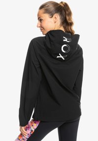 Black hooded jacket with a sleek, smooth texture. Features a prominent white logo on the back and elastic cuffs. Simple, functional design.