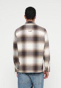 Rutete flanellskjorte i hvite, brune og beige toner. Har knappede mansjetter, et bakemerk og en avslappet passform med en myk tekstur.