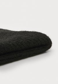 Schwarzer Strickstoff mit einem strukturierten, gewebten Muster, gefaltet und zeigt abgerundete Kanten sowie eine weiche, flauschige Oberfläche.
