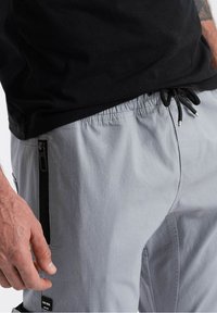 Grijze cargoshorts met een elastische tailleband, zwarte trekkoord en zijzakken met rits. De stof lijkt glad en licht van gewicht.