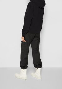 Černá mikina s těsným střihem, doplněná o černé cargo kalhoty s kapsami. Bílé boty po lýtka s texturovanými podrážkami dokončují vzhled.