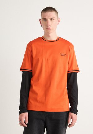 Orange kortærmet t-shirt med et sort langærmet lag under. Har rund halsudskæring og broderet logo på brystet.