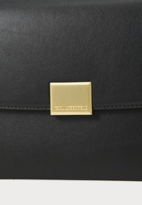 Svart läderclutch med en texturerad yta, utrustad med ett rektangulärt magnetstängning i guldton och prägling av varumärket på den metalliska detaljen.