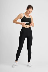 Black leggings with a high waistband and mesh panel, paired with a dark green sports bra featuring a white trim. Light gray sneakers.