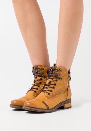 Vaaleat nilkkurit, joissa on teksturoitu pinta, kuviollinen pinta, ruskeat nauhat ja sivuvetoketju. Paksu korko ja korostetut ompeluyksityiskohdat.