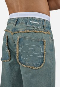 Lichtblauwe denim shorts met rafelige randen, contrasterende stiksels en opvallende grote achterzakken met een geometrisch patroon.