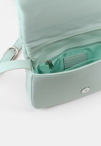 Miętowozielona torebka noszona przez ramię wykonana z gładkiej ekoskóry, z zatrzaskiem oraz pojemnym wnętrzem z kieszenią na zamek.