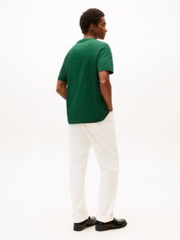 Camiseta verde de manga corta con cuello redondo, combinada con pantalones rectos blancos y zapatos negros, vista desde la parte posterior.