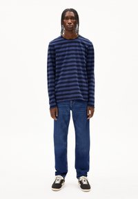 Marineblauwe gestreepte T-shirt met lange mouwen, gecombineerd met rechte blauwe jeans en zwarte sneakers met witte accenten.