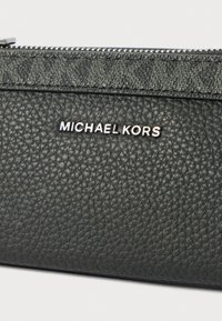 Czarny skórzany portfel z teksturowaną powierzchnią, zamkiem błyskawicznym i srebrnym logo "Michael Kors". Projekt jest elegancki o minimalistycznym stylu.
