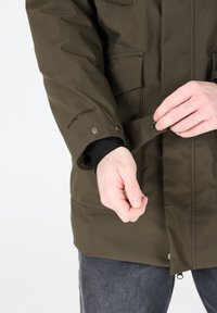 Olivgrön jacka med en slät, texturerad yta. Har tryckknappar och "W.P.R.O 10000"-logotyp på ärmen. Praktisk design med fickor.