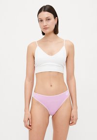 Hvit bomulls-bralette med tynne stropper og V-hals, parret med lyse rosa bomullsundertøys med hvit midjebånd og logo.