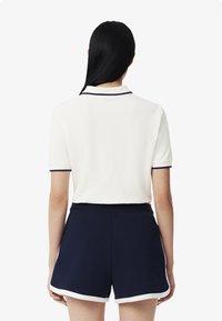 Vit polotröja med marinblå detaljer, kort ärm och krage, matchad med marinblå shorts som har vit piping längs nederkanten.