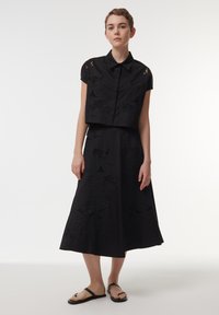 Camisa corta negra con mangas cortas, que presenta intrincados diseños recortados. Falda negra a juego con patrones bordados detallados. Chanclas de goma.