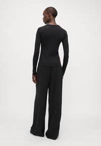 Black long-sleeve top with a fitted design and crew neckline, paired with wide-leg black pants. Smooth texture, minimal detailing.