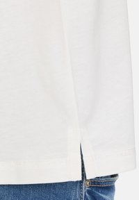 Hvid bomulds T-shirt med rund søm, sideslids og en glat tekstur, parret med blå denim jeans med en sølvknap.