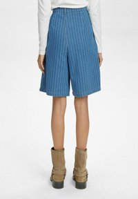 Kék csíkos farmer rövidnadrág, egyenes sziluettel. Barna bokacsizmával párosítva, amelyen csatos díszítés található.