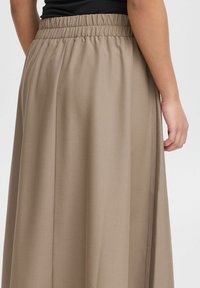 Long beige skirt with a gathered elastic waistband, featuring a smooth texture and a subtle sheen. Plain design without patterns or accents.
