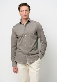 Camisa de franela gris de manga larga con botones, hecha de algodón suave, que presenta un cuello clásico y un brillo sutil, combinada con pantalones crema claros.